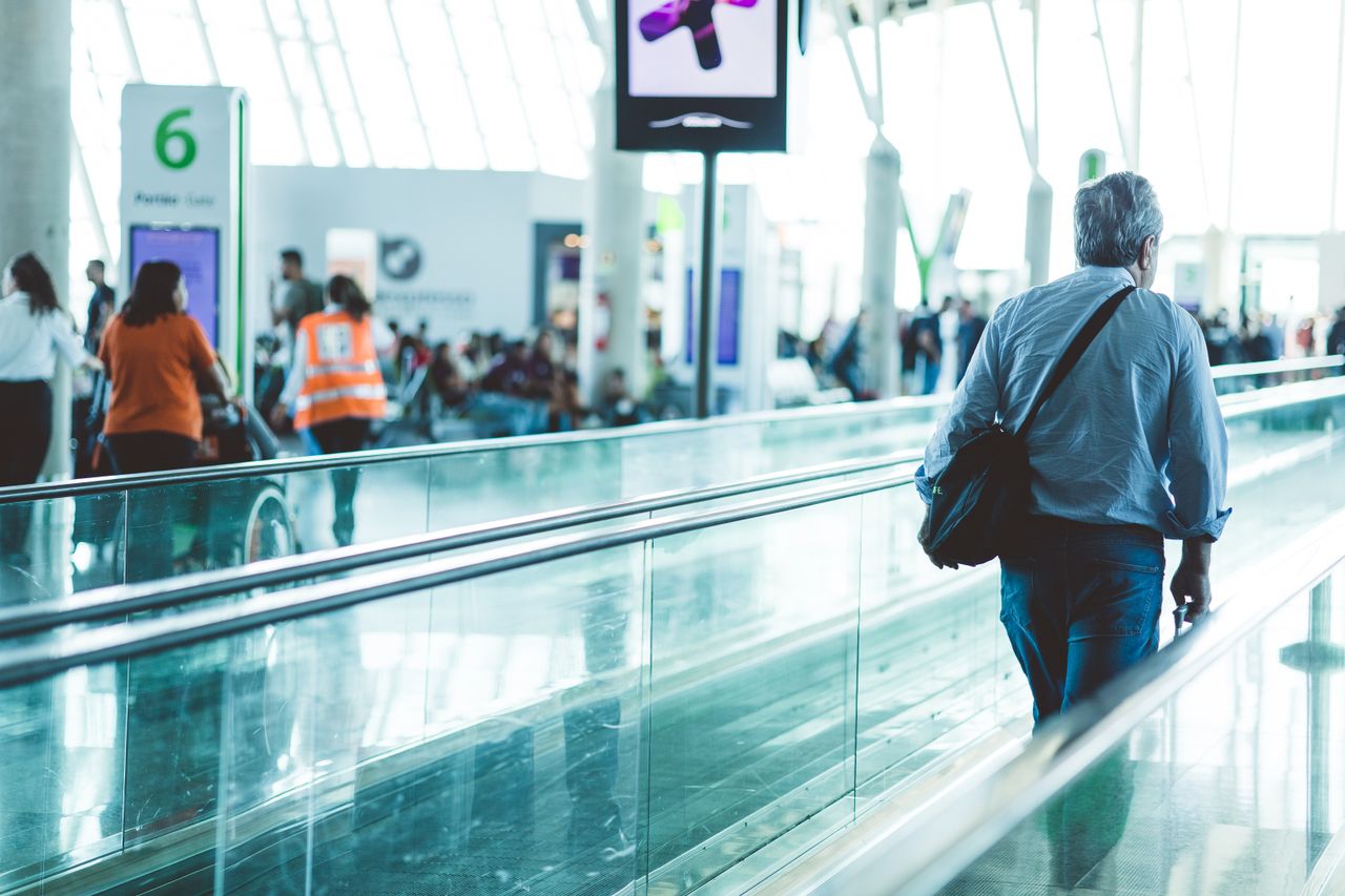 A bustling airport scene with travelers on a moving walkway in a modern terminal.