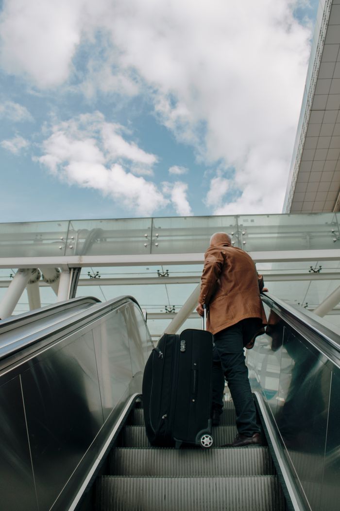 Crafting Captivating Headlines: Your awesome post title goes here Adult male riding an escalator with luggage in an airport, traveling with bright sky overhead.